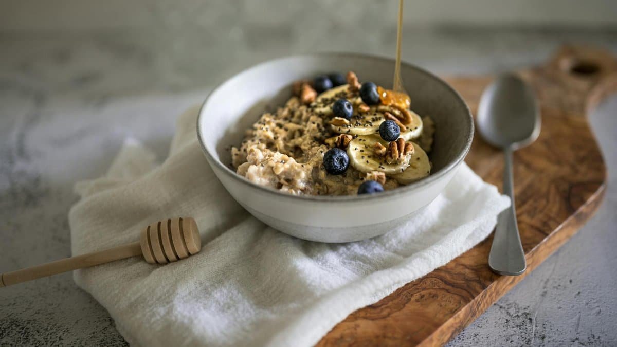 A ceramic bowl of oatmeal topped with blueberries, bananas, and walnuts on a wooden tray.