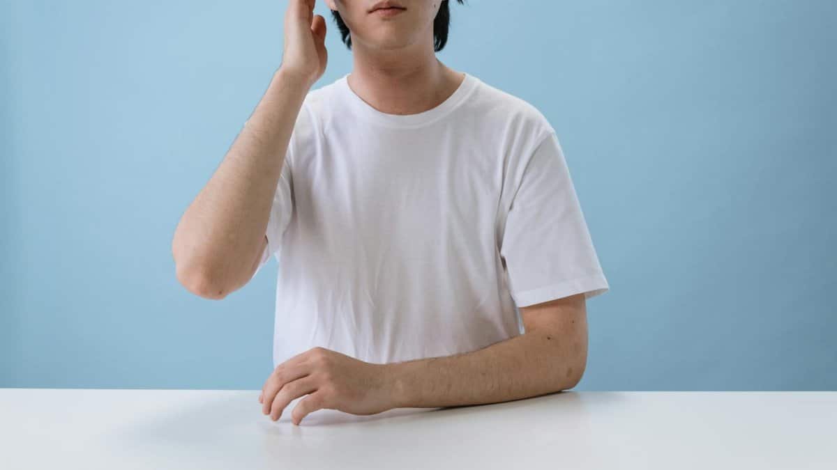 A man in a blank white t-shirt sits pensively against a blue background.