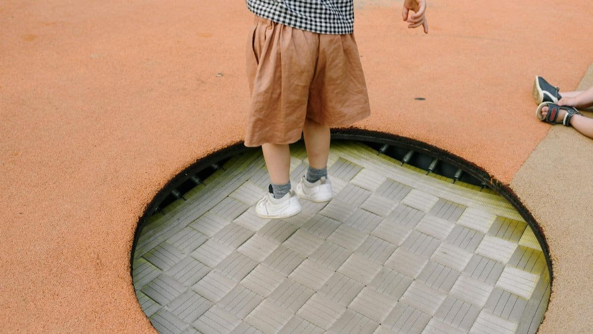 A young child enjoys jumping on an outdoor playground trampoline, capturing the essence of playful childhood fun.