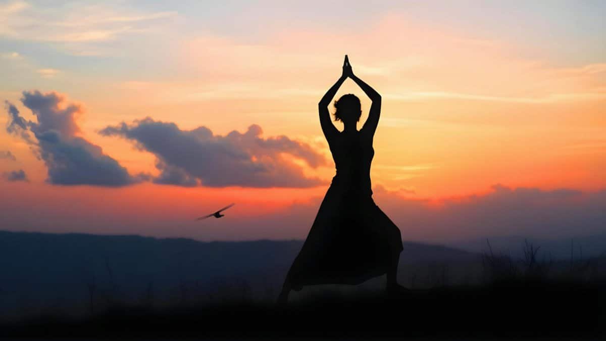 Silhouette of a woman practicing yoga during a serene sunset outdoors.