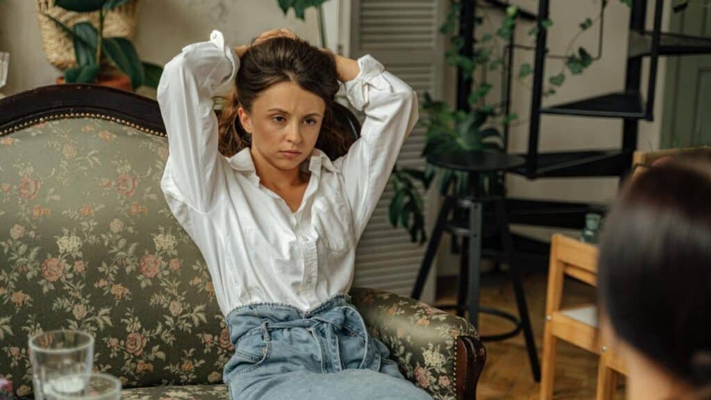 Woman sitting on a floral couch, appearing deep in thought in a cozy living room setting.