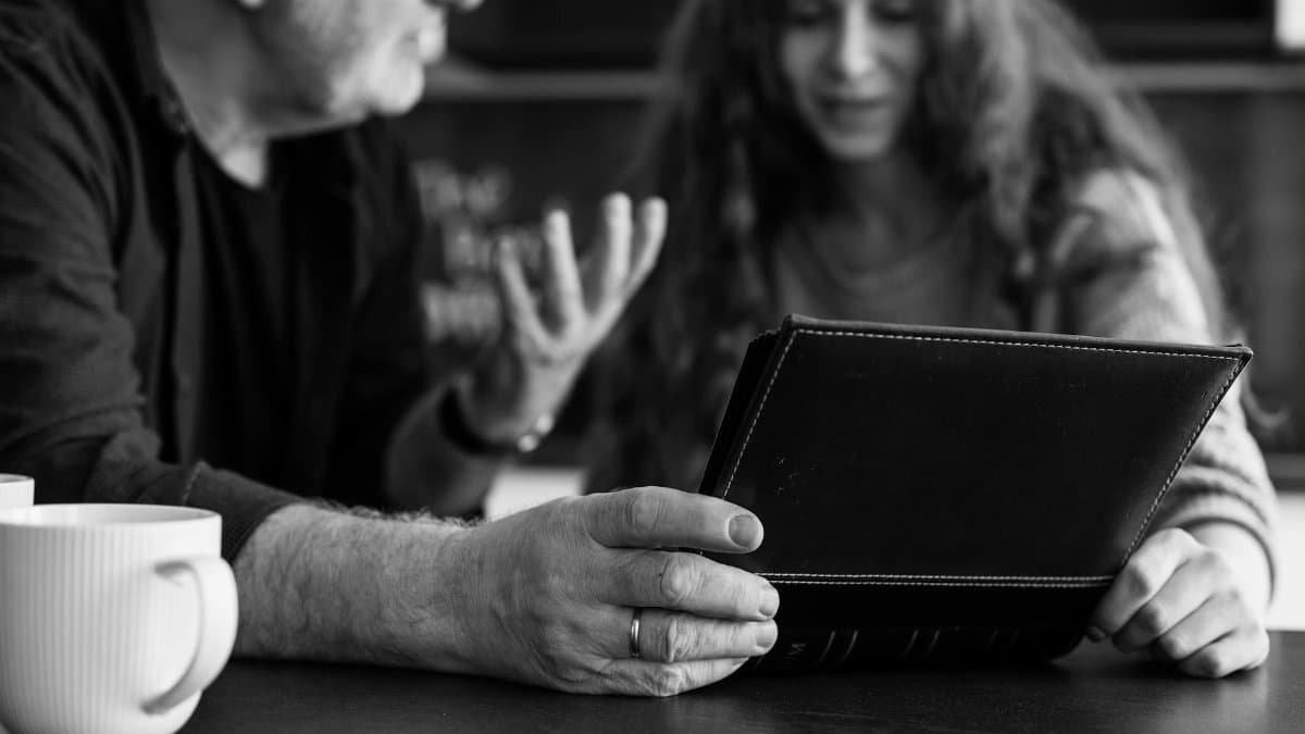 A monochrome image of two individuals looking at a photo album while conversing.