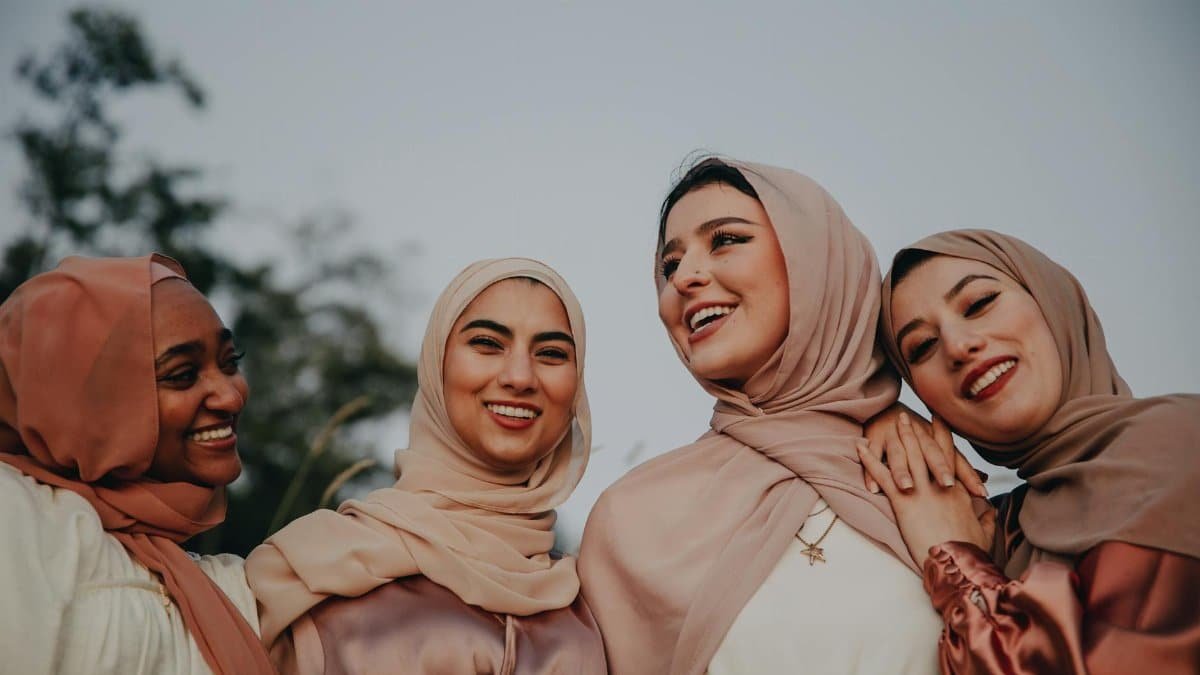Four diverse women in hijabs laughing together outdoors, embracing friendship.