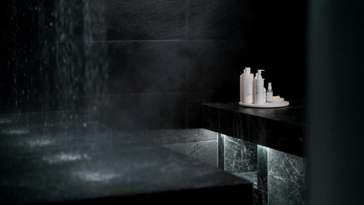 Luxurious modern bathroom with sleek black tiles and a set of cosmetic bottles under soft lighting.