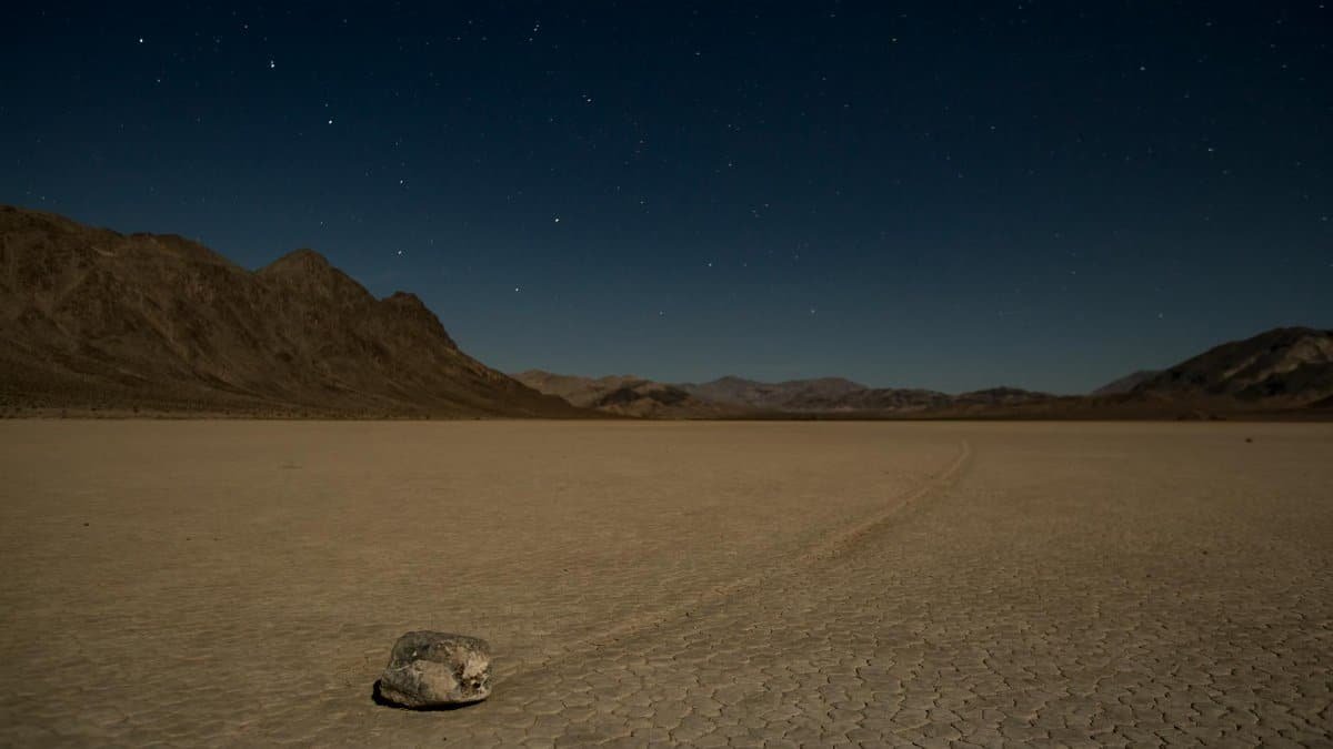 A solitary sailing stone on the vast Racetrack Playa under a starry night sky in Death Valley.