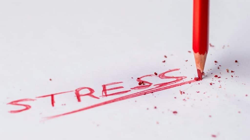 Close-up of a red pencil writing 'stress' on paper, symbolizing pressure and creativity.