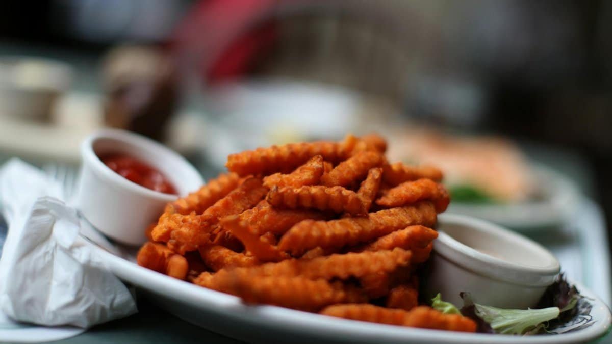 Crinkle-cut sweet potato fries served with ketchup on a white plate, ideal for food lovers.