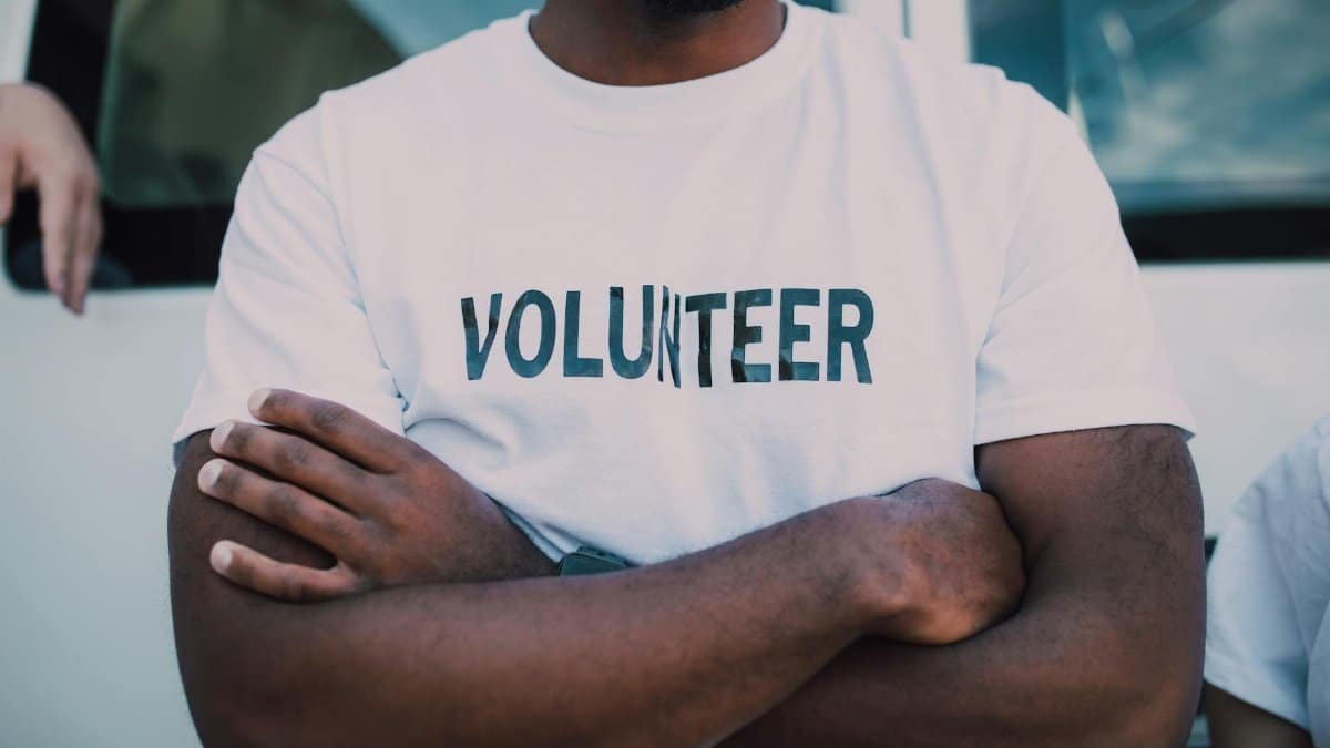 A close-up of a person wearing a volunteer shirt with arms crossed, promoting community service.