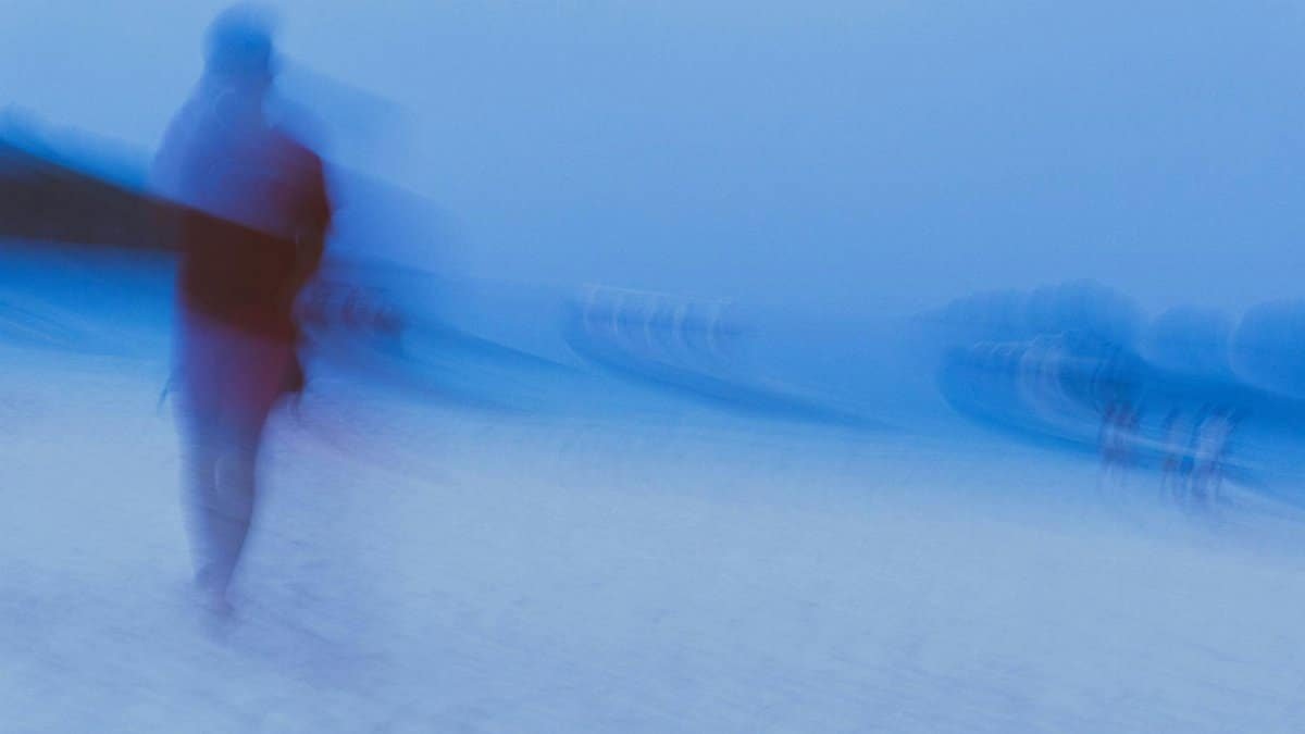 Artistic capture of a blurred silhouette walking on a beach with blue tones and sand.