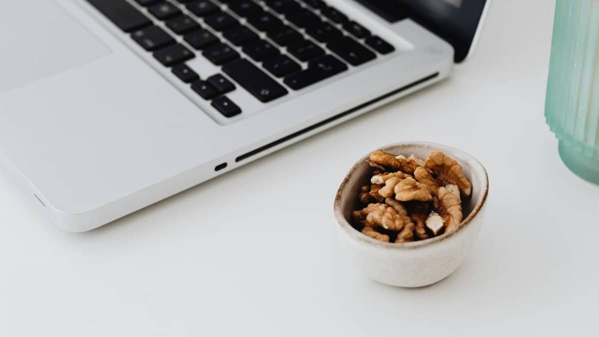 A minimalistic work desk setup featuring a laptop and a bowl of healthy walnuts for snacking.