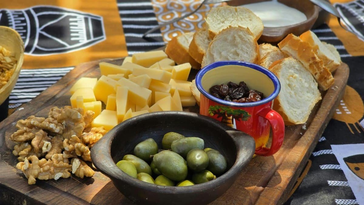 A rustic picnic setup with cheese, olives, and bread on a wooden board. Perfect for outdoor gatherings.