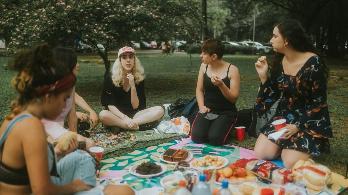 A group of women enjoying a picnic at the park with food, drinks, and nature.