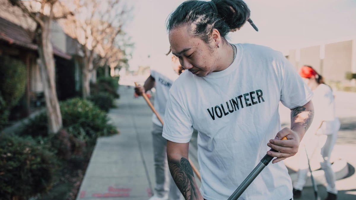 Volunteers in white shirts clean a city sidewalk, promoting community spirit and teamwork.