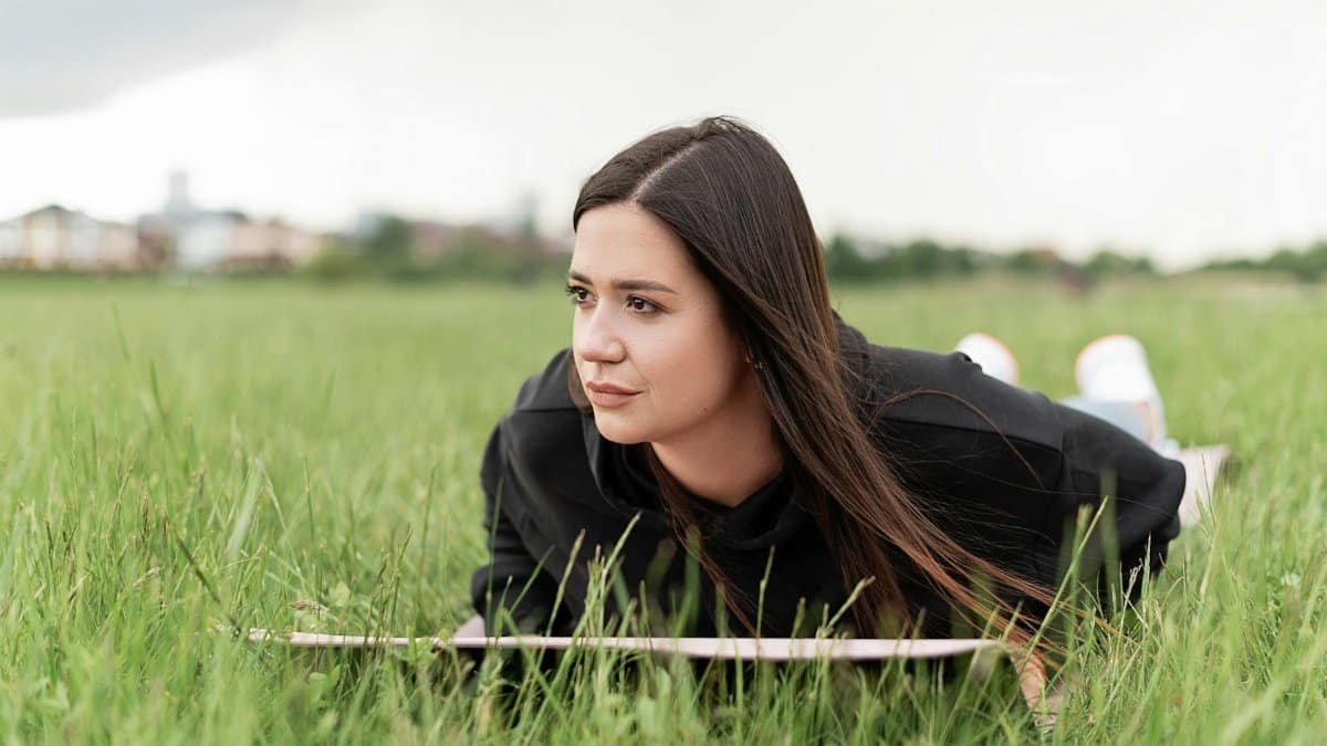 Young woman lying on a yoga mat in a grassy field, enjoying a serene outdoor moment.
