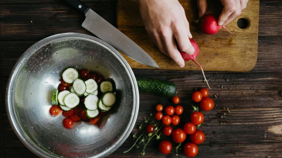 Hands preparing fresh vegetable salad with cherry tomatoes, cucumbers, and radishes on a wooden board.
