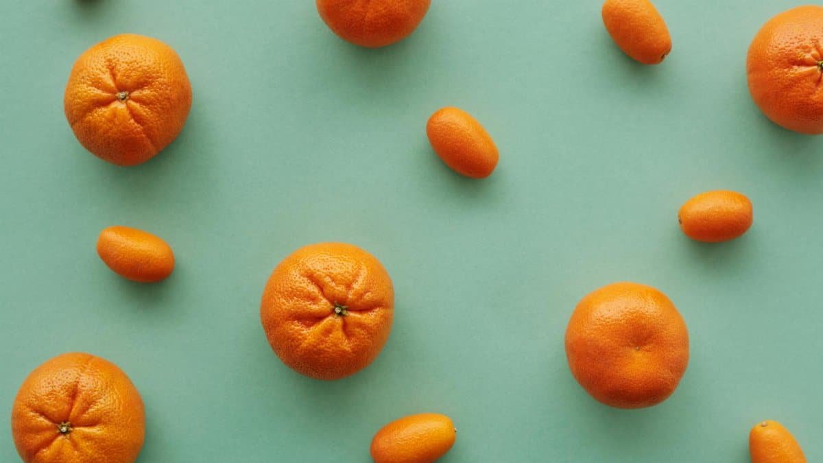Scattered oranges and kumquats in a flat lay on a green backdrop, emphasizing fresh citrus fruits.