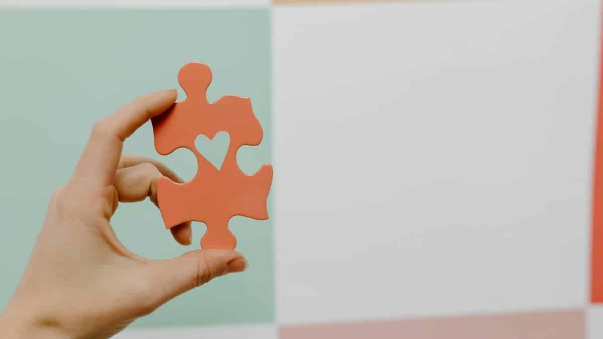 Close-up of a hand holding a heart-shaped puzzle piece against a colorful background.