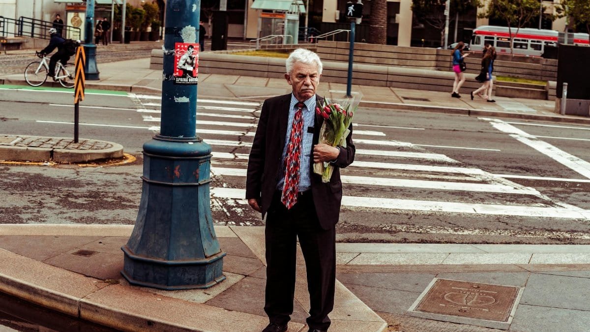 Elderly man holding flowers at a San Francisco crosswalk, vibrant urban scene.