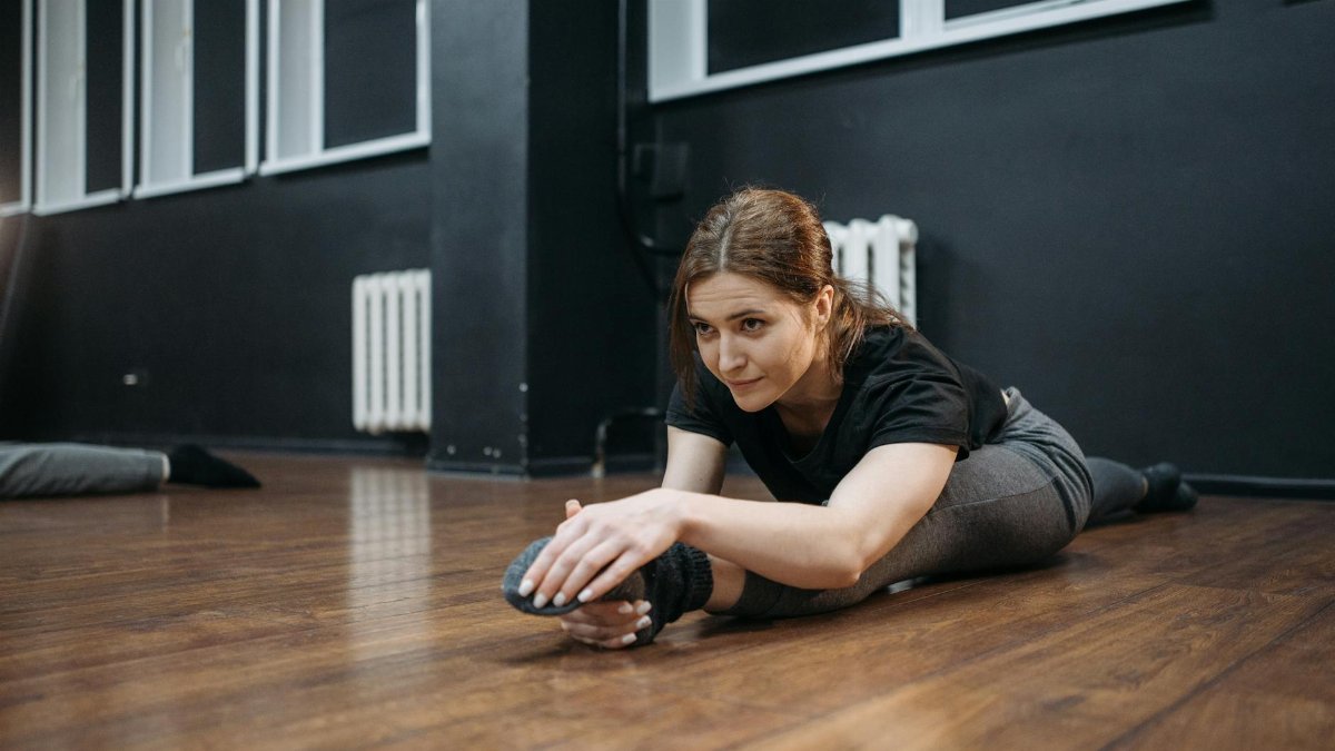 A woman performs a stretch on a wooden floor in a dance studio, showcasing flexibility and fitness.