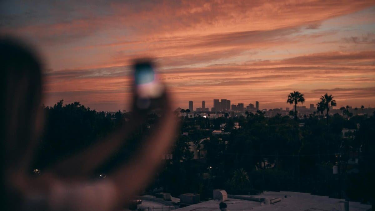 A person photographing the Los Angeles skyline during a vibrant sunset.