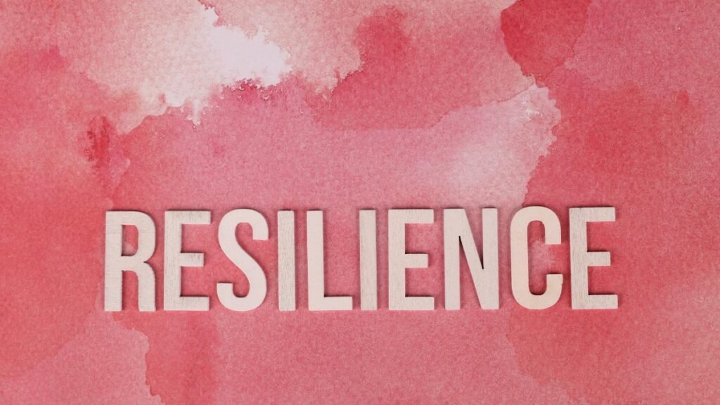 Word 'Resilience' on a pink watercolor background, symbolizing strength.