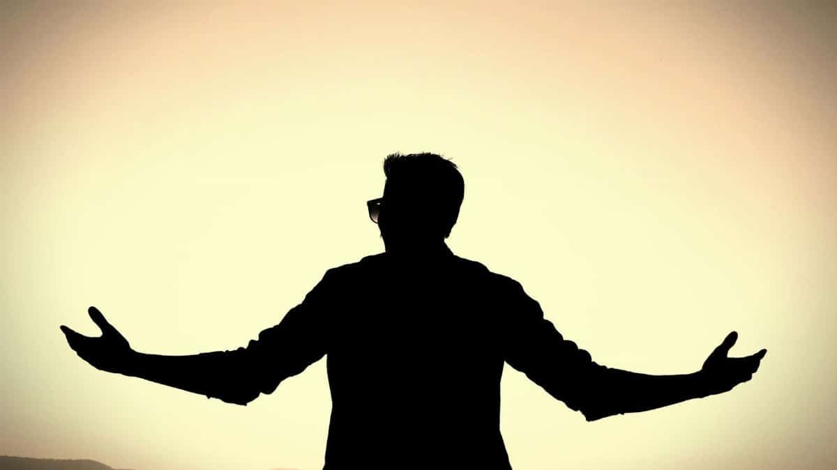 Silhouette of a man with open arms against a vibrant sunset background, symbolizing freedom and peace.