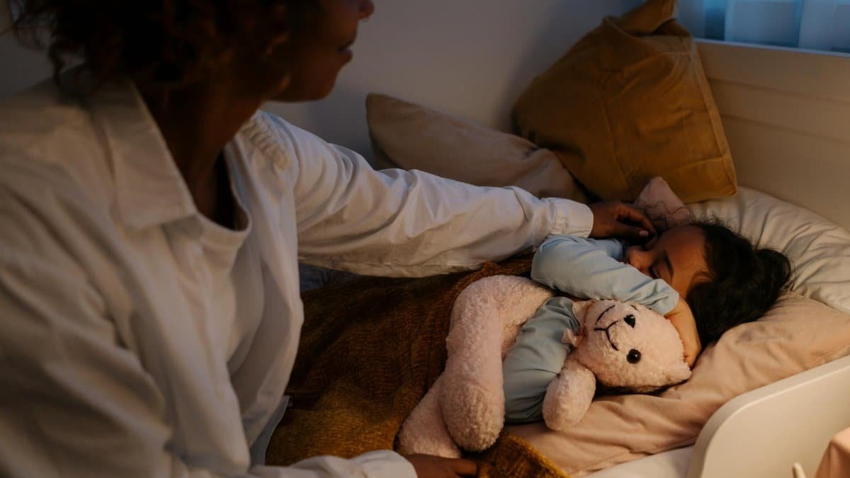 A tender moment of a mother tucking her child in for a cozy night's sleep with a teddy bear.