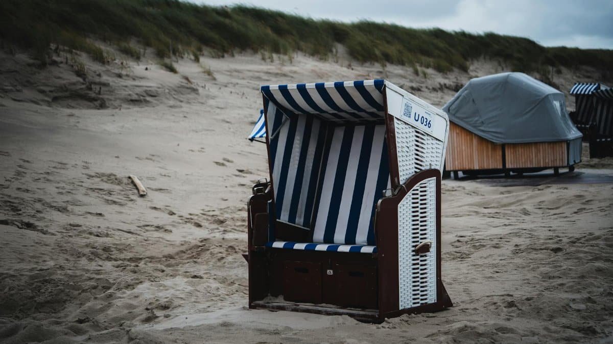 Beach hut with blue and white stripes on a sandy coastline under cloudy skies.