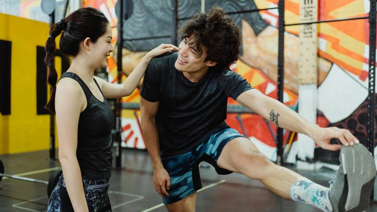 Asian couple exercising and stretching together in a vibrant gym setting, fostering health and fitness.