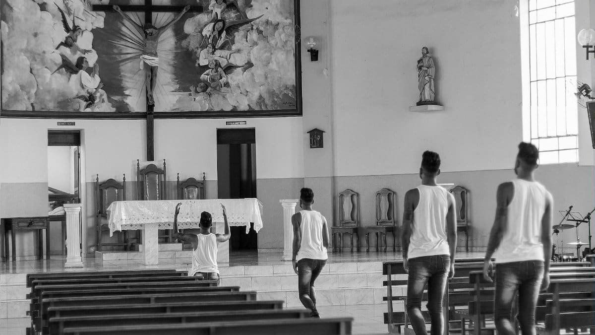 A group of individuals praying in a Catholic church, captured in grayscale.