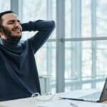 Man leaning back in office chair, appearing relaxed amidst a busy workday, reflecting stress management.