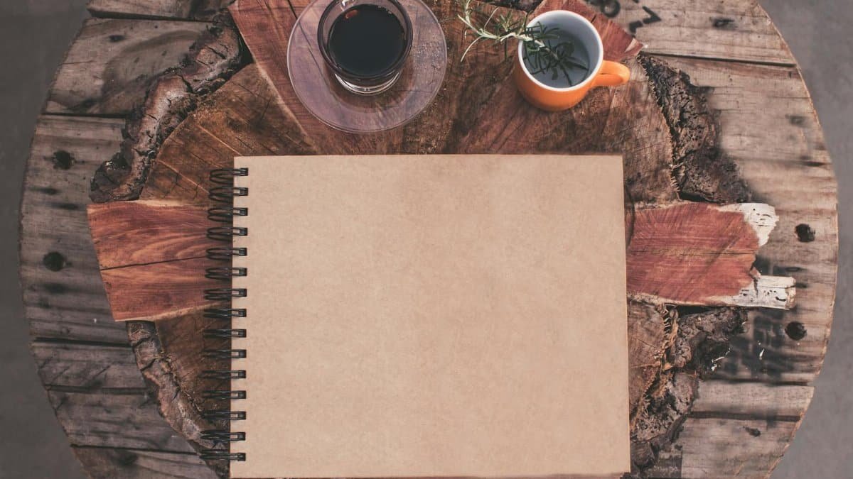 Top view of a rustic table with a blank notebook, coffee, and herbal tea.