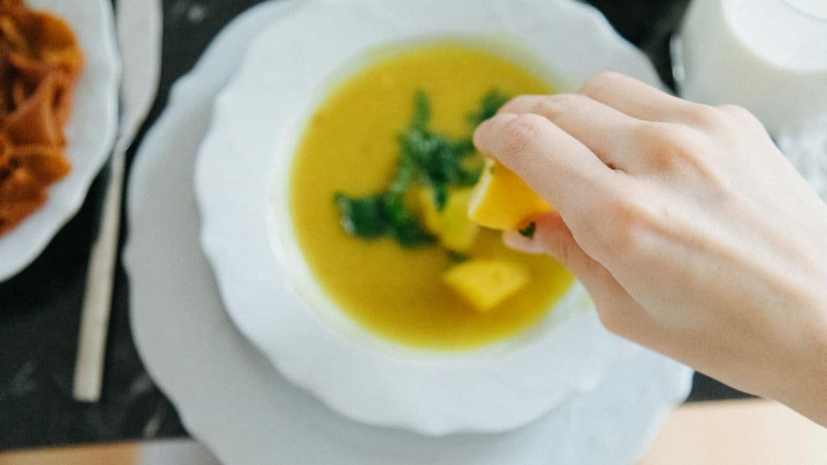 Hand squeezing lemon over lentil soup, enhancing flavor in traditional Turkish setting.
