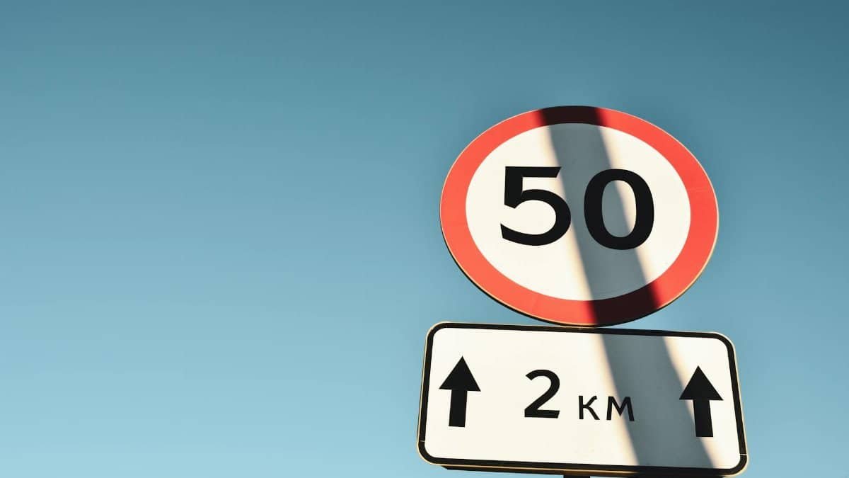 Clear speed limit and distance sign against blue sky, offering guidance and information.