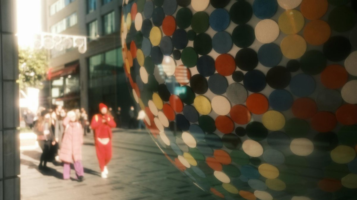 Vibrant circles on glass art installation reflecting pedestrians in a busy urban area.