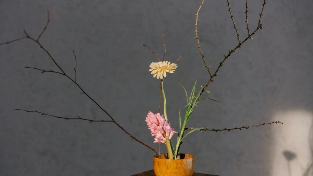 A minimalist floral arrangement in a wooden vase with branches and soft lighting.