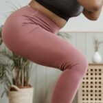 Close-up view of a woman squatting indoors wearing pink leggings and black top.