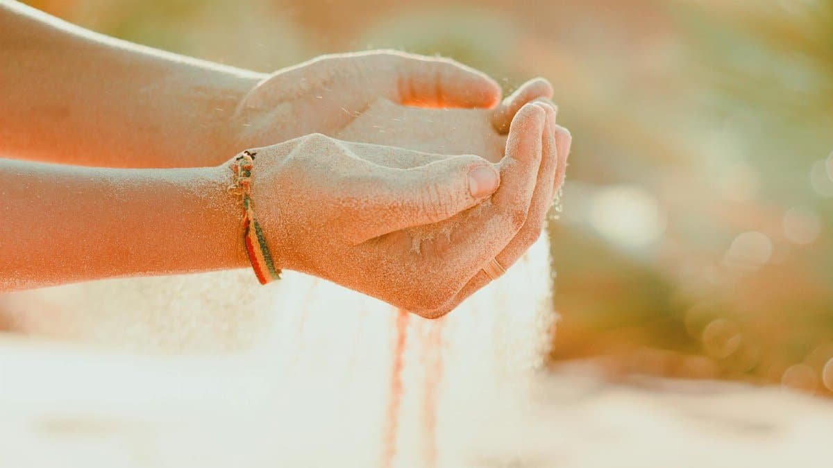 A warm close-up of hands cupping sand outdoors, symbolizing time and nature.