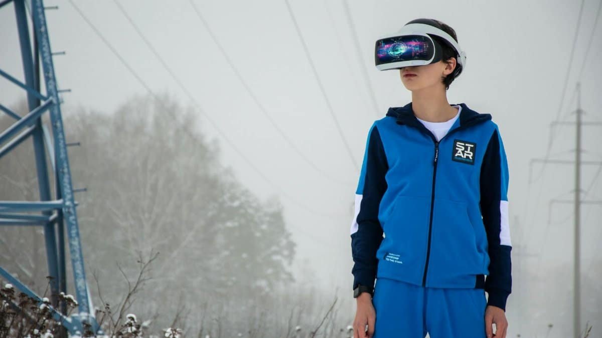 A teenager wearing VR goggles in a blue tracksuit, experiencing virtual reality in a snowy landscape.