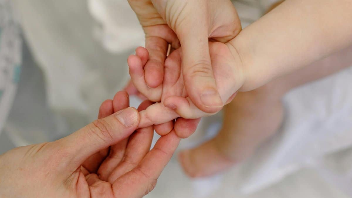 Close-up of an adult giving a gentle massage to a baby's hand, showcasing tender care and nurturing touch.