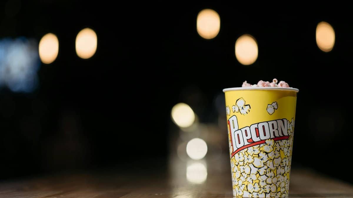 Close-up of popcorn in a yellow cup on a wooden table with blurred lights in the background, creating a cinematic ambiance.