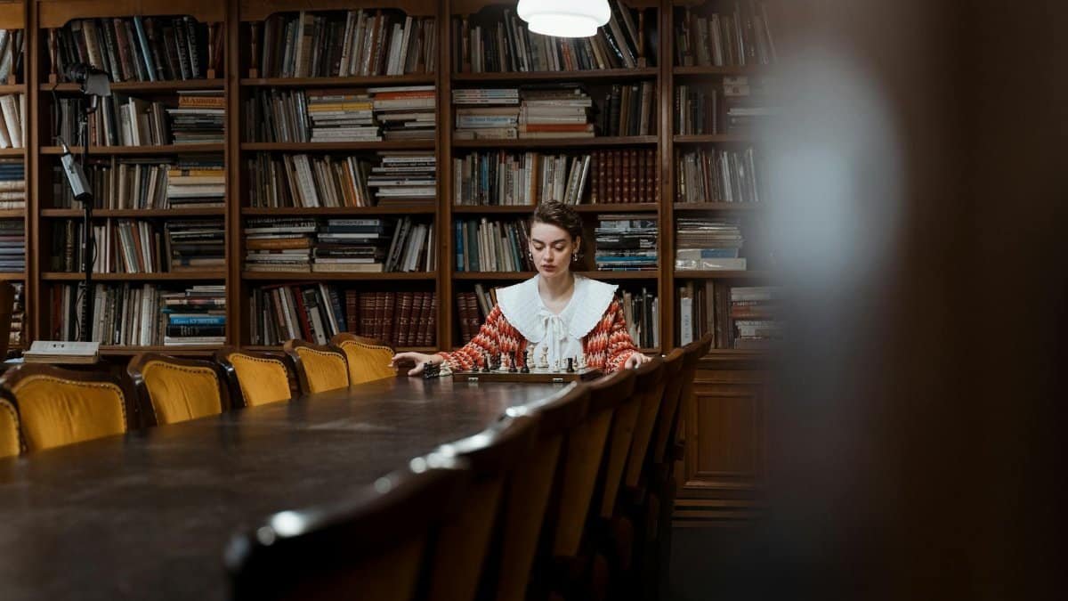 A woman deep in thought, seated in a vintage library with bookshelves.