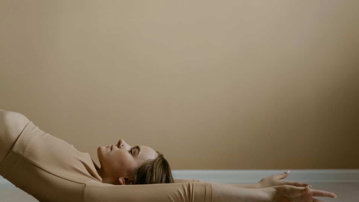 Woman in calm yoga pose, arms extended, in neutral setting.