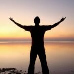 A person joyfully embracing the sunrise over a calm ocean, symbolizing freedom and solitude.