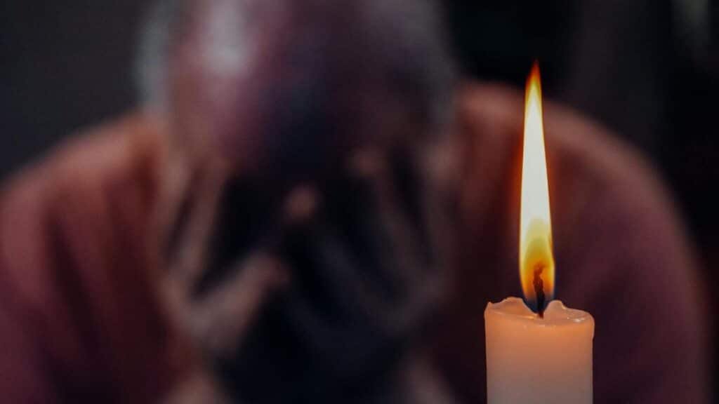 A senior adult in an emotional moment lit by a candle, symbolizing reflection and grief.