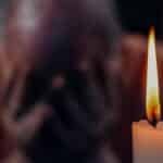 A senior adult in an emotional moment lit by a candle, symbolizing reflection and grief.