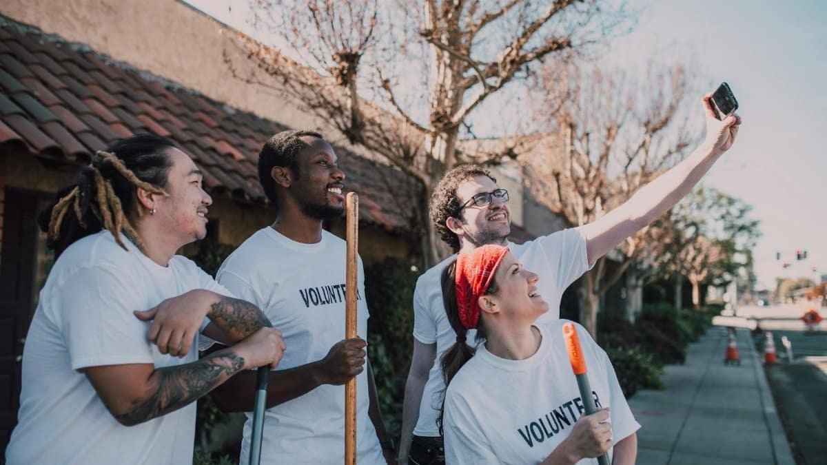 A diverse group of volunteers wearing white shirts and taking a selfie outdoors.