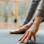 A person stretches their hand and foot on a yoga mat indoors, focusing on wellness.