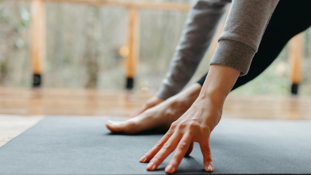 A person stretches their hand and foot on a yoga mat indoors, focusing on wellness.