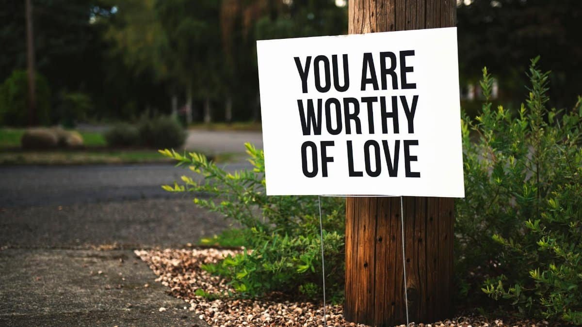 A positive message sign "You are worthy of love" in a park setting.